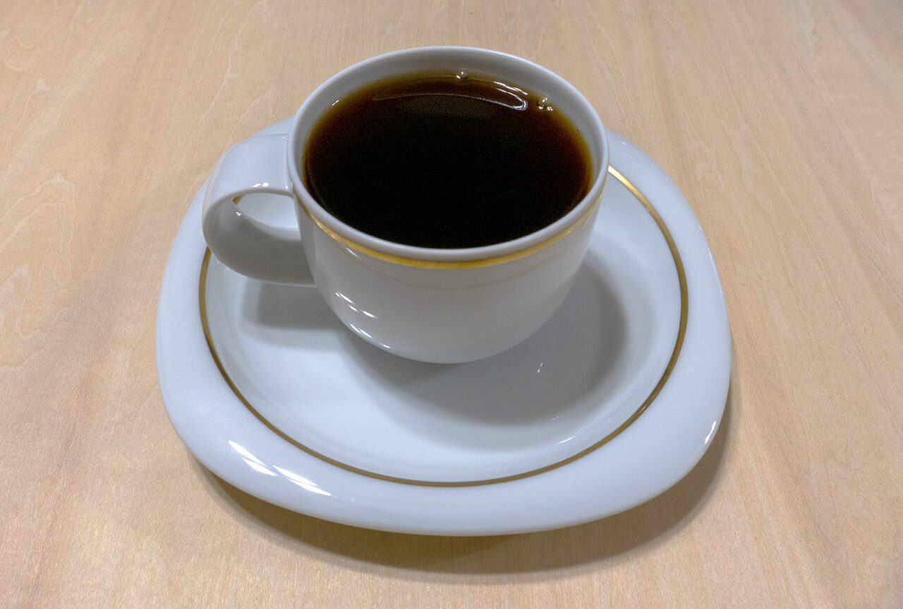 木のテーブルに置いた金縁の白いカップとソーサーに入ったコーヒー